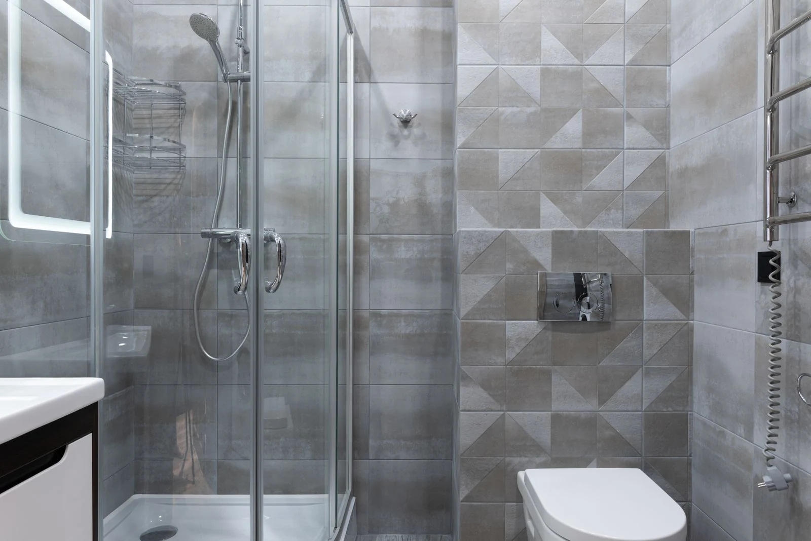 Contemporary shower cabin with glass walls between metal rack on tiles and washstand in house